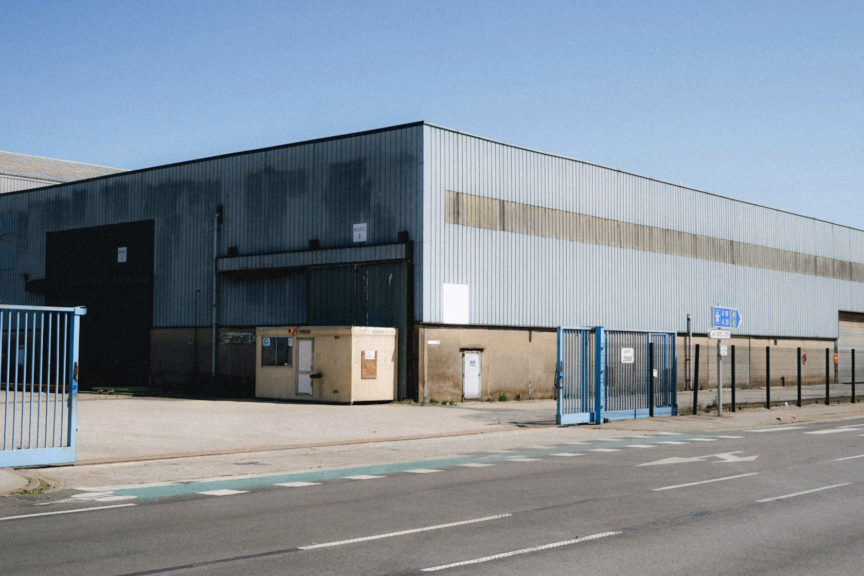 Nave industrial de gran tamaño con portones azules junto a una carretera